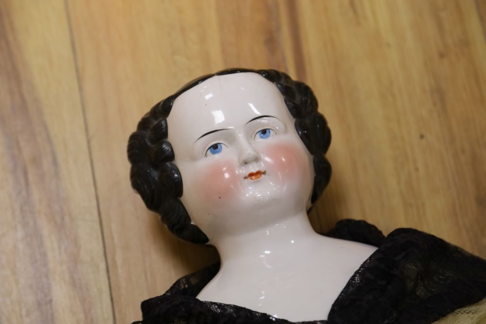 A large unusual glazed china shoulder head doll, circa 1850. Short moulded hair. Sawdust filled cloth body, original boots, wearing